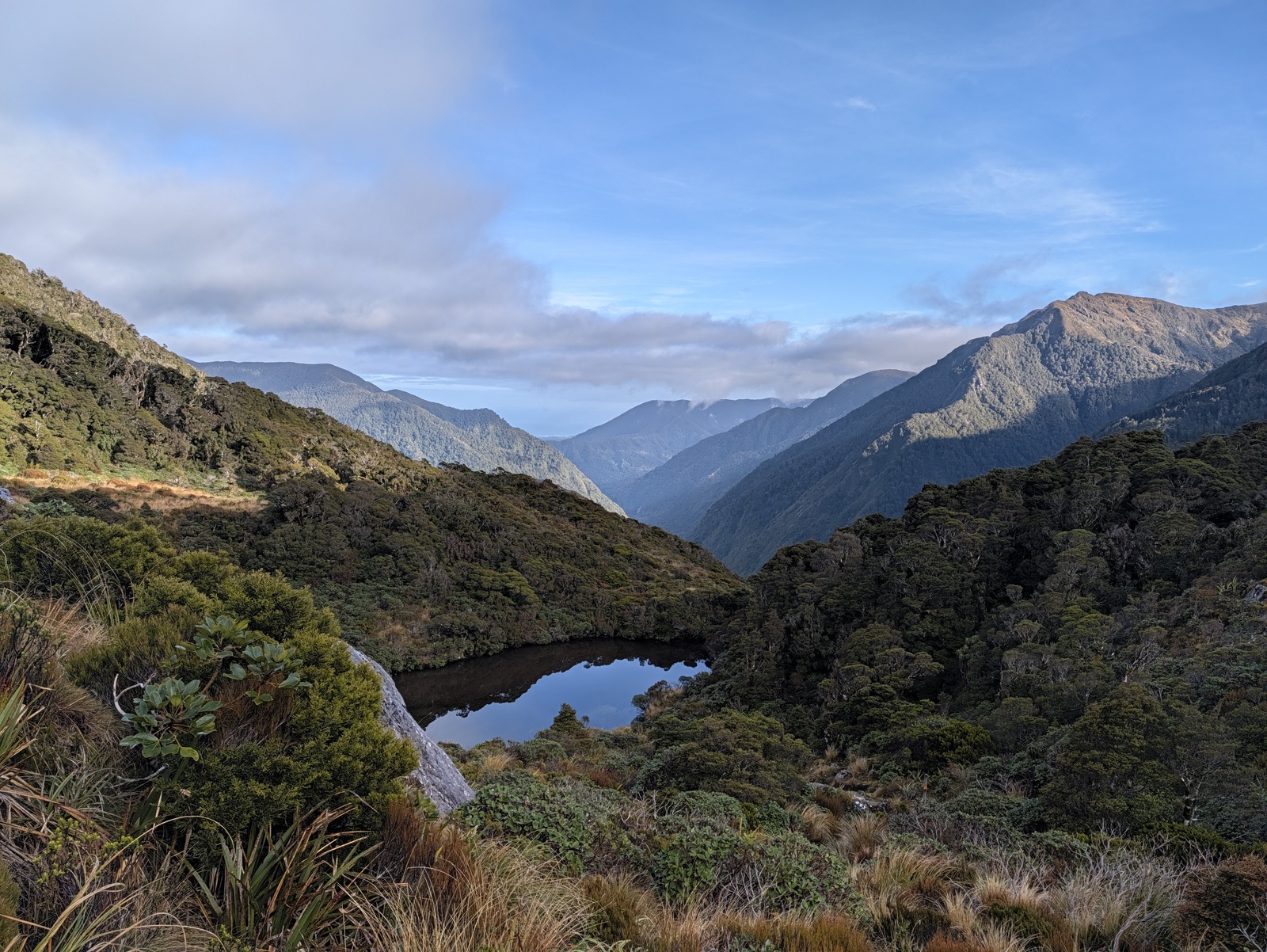 View from Little Wanganui Saddle over Saddle Lake, down the Little Wanganui River valley to the ocean; the beach of Karamea Bight can be seen in the distance